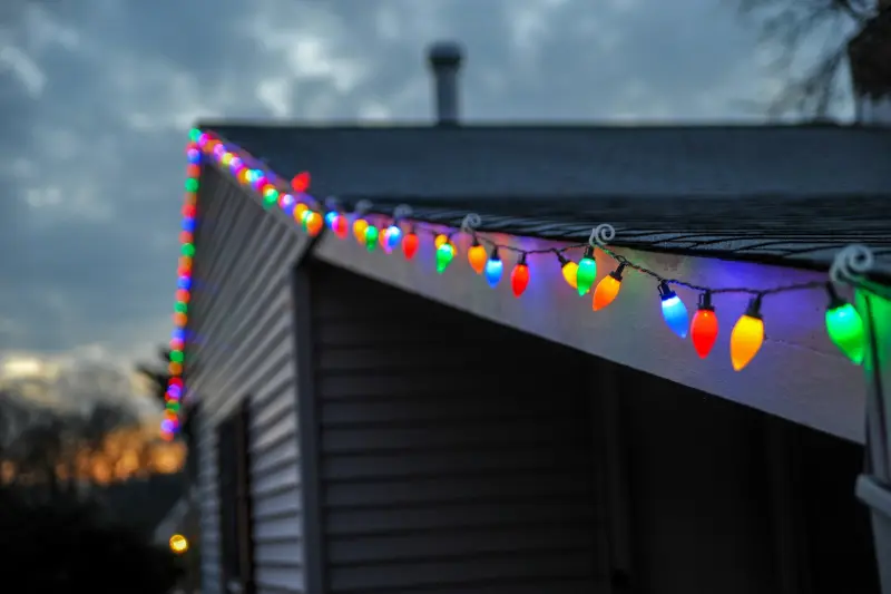 Warm white Christmas lights along a roofline at dusk